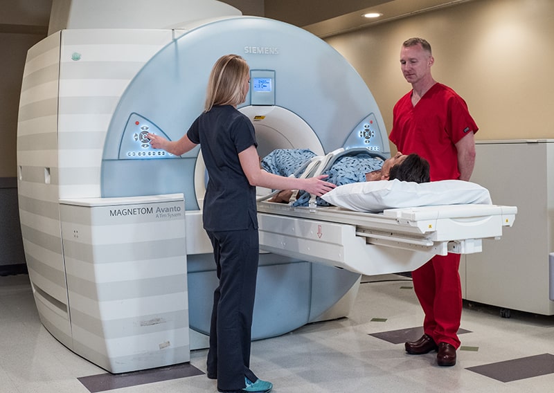 Two ARA Austin technicians stand on either side of a patient about to receive an MRI scan.