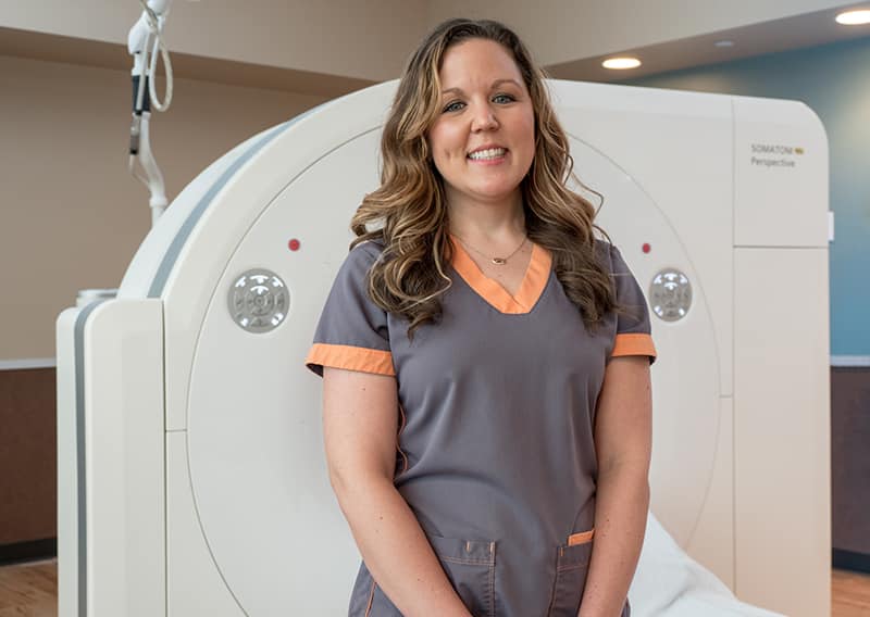 An ARA CT scan technician stands next to a scanning machine.