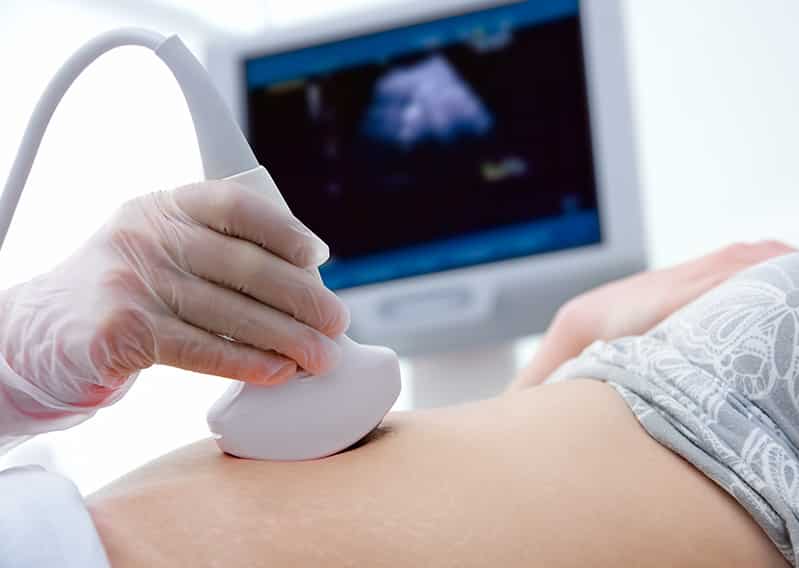 A technologist gliding an ultrasound wand over a patient's abdomen.
